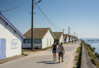 Deux personnes marchent près des cabanes colorées au bord de l’eau à Arès, Nouvelle-Aquitaine, France.