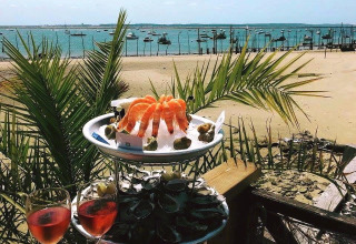 Meeresfrüchte und Roséwein auf einer Terrasse mit Meerblick und Booten nahe Arès, Nouvelle-Aquitaine, Frankreich.