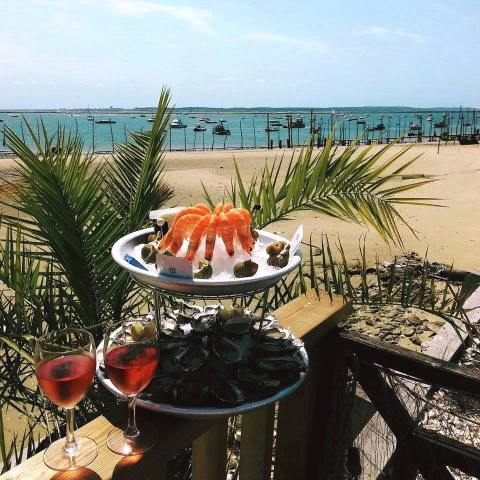 Mariscos y vino rosado en una terraza con vista a la playa y barcos cerca de Arès, Nouvelle-Aquitaine, Francia.