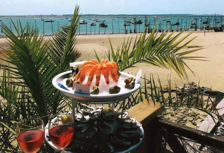 Schaal- en schelpdieren en roséwijn op terras met uitzicht op strand en boten bij Arès, Nouvelle-Aquitaine, Frankrijk.
