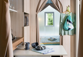Moderne glampingverblijf met compacte keuken, eettafel en slaapkamer, gescheiden door gordijnen.