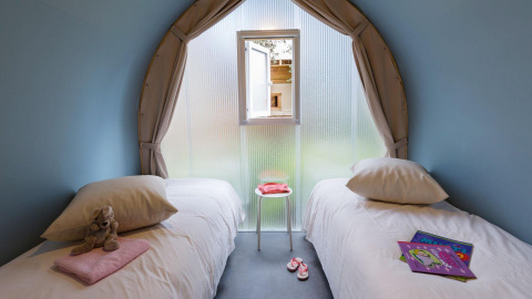 Knusse glamping kamer met twee eenpersoonsbedden, knuffel, kinderboeken, raam en slippers.