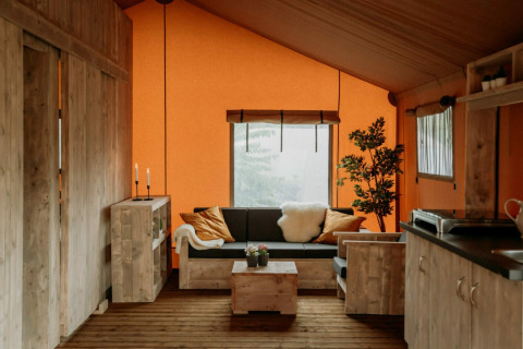 Gemütlicher Wohnbereich im Holiday Park Mölke mit Holzmöbeln und oranger Zeltwand in Overijssel, Niederlande.