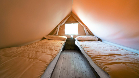 Twee eenpersoonsbedden in een glampingtent met houten vloer en raam, ideaal voor een comfortabele belevenis.