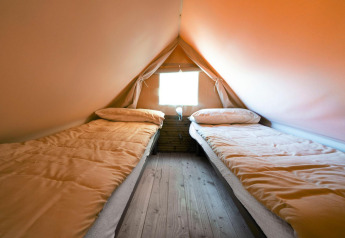 Dos camas individuales en una cómoda tienda de glamping con suelo de madera y ventana, ideal para relajarse.