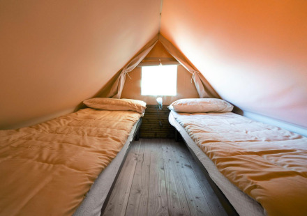 Twee eenpersoonsbedden in een gezellige glamping tent met houten vloer en raam, comfortabel in de natuur.