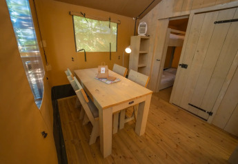 Indretning af et glamping-telt med et træbord, fire stole og et kig til soveplads i baggrunden.