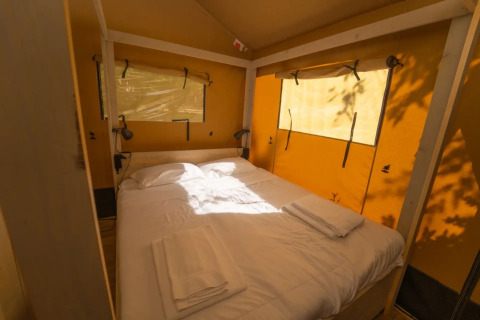 Intérieur d'une tente glamping avec lit double, draps blancs et lumière naturelle à travers les fenêtres.