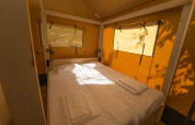 Interno di una tenda glamping con letto matrimoniale, lenzuola bianche e luce naturale dalle finestre.