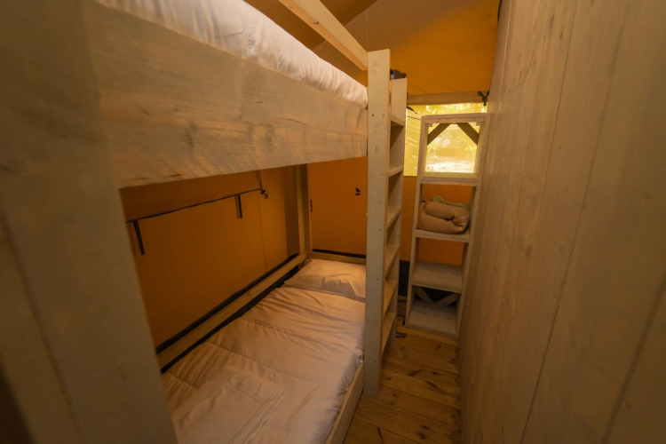 Interior view of a glamping accommodation with wooden bunk beds, shelving, and a warm, cozy ambiance.