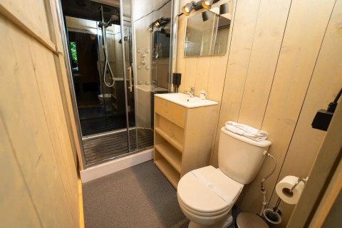 Baño moderno en alojamiento glamping con ducha de cristal, inodoro, lavabo y paredes de madera.
