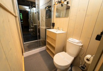 Moderne badeværelse i glampingindkvartering med brusedør, toilet, håndvask og træpanelvægge.