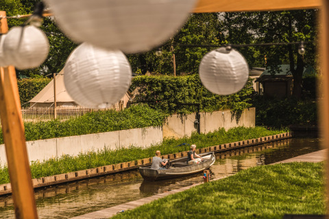 Dos personas navegan en un bote por un canal en Holiday Park Mölke, Países Bajos, con farolillos.