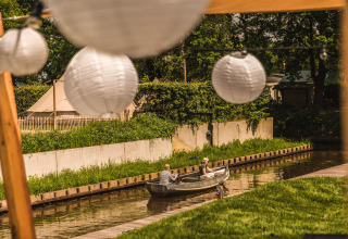Twee mensen varen in een bootje op een kanaal bij Holiday Park Mölke, met lampionnen op de voorgrond.