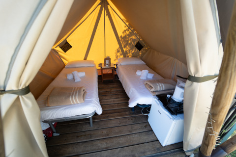 Deux lits simples dans une tente glamping de luxe avec plancher en bois, mini-réfrigérateur et serviettes.