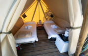 Deux lits simples dans une tente glamping de luxe avec plancher en bois, mini-réfrigérateur et serviettes.
