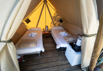 Dos camas individuales en una tienda glamping lujosa con suelo de madera, nevera y toallas enrolladas.