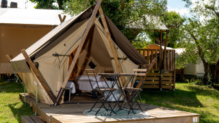 Junior Safari Tent mit Holzterrasse, kleinen Tisch und Stühlen in grünem, sonnigem Campingbereich.
