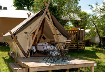 Tienda Junior Safari con terraza de madera, mesa y sillas al aire libre, en un entorno campestre soleado.