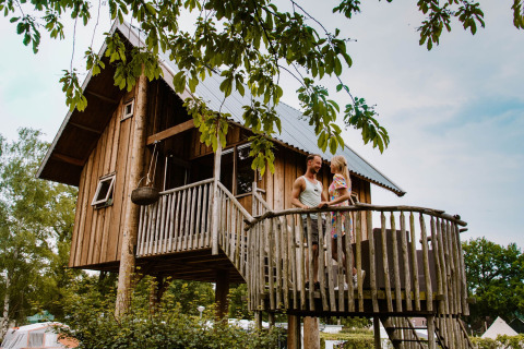 Un couple profite du balcon d'une cabane dans les arbres au Holiday Park Mölke à Overijssel, Pays-Bas, entouré de verdure.