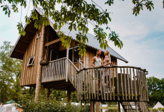 Een koppel geniet op het terras van een boomhut in vakantiepark Mölke in Overijssel, Nederland, tussen de bomen.