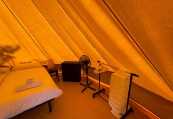 Vista interior de la Bell Tent en Sivinos Camping Boutique, Italia, con cama, silla y ventilador.