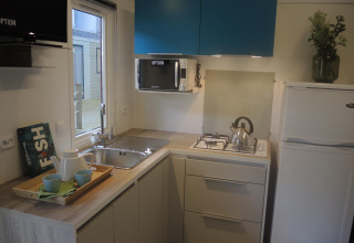 Angolo cottura moderno per glamping con lavello, fornello a gas, frigo, microonde e pensili blu.