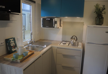Angolo cottura moderno per glamping con lavello, fornello a gas, frigo, microonde e pensili blu.