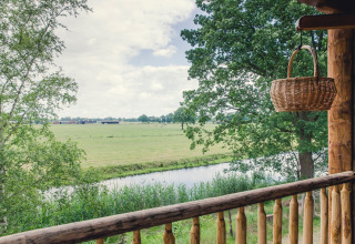 Blick von einem Balkon mit Korb auf Bäume, Fluss und Wiesen im Ferienpark Mölke, Overijssel, Niederlande.