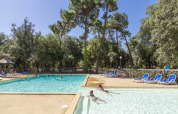 Buitenzwembad met ligstoelen en gasten bij Flower Camping Monplaisir, omringd door bomen in Nouvelle-Aquitaine.