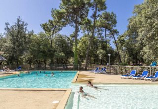 Buitenzwembad met ligzetels en gasten bij Flower Camping Monplaisir, omringd door bomen in Nouvelle-Aquitaine.