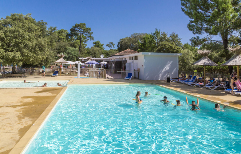 Buitenzwembad met vakantiegangers, ligstoelen en parasols bij Flower Camping Monplaisir, Nouvelle-Aquitaine.