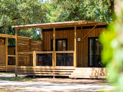 Træhytte med terrasse omgivet af træer på Flower Camping Monplaisir, feriepark i Nouvelle-Aquitaine, Frankrig.