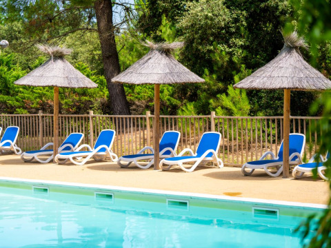 Piscine avec transats bleus et parasols en paille au Flower Camping Monplaisir en Nouvelle-Aquitaine, France.