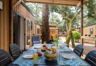 Ontbijttafel buiten aan een chalet op Flower Camping Monplaisir, omringd door bomen en vakantiehuisjes.