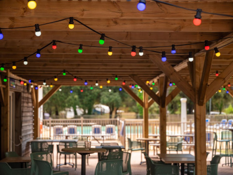 Terraza exterior con mesas y luces de colores en Flower Camping Monplaisir, Nouvelle-Aquitaine, Francia.