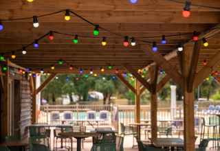 Outdoor patio seating under a wooden pergola with colorful string lights at Flower Camping Monplaisir in France.