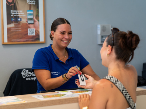Receptionist hands guest a keycard at Flower Camping Monplaisir holiday park in Nouvelle-Aquitaine, France