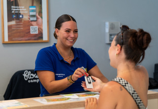 Receptionist udleverer nøglekort til gæst på Flower Camping Monplaisir feriepark i Nouvelle-Aquitaine, Frankrig