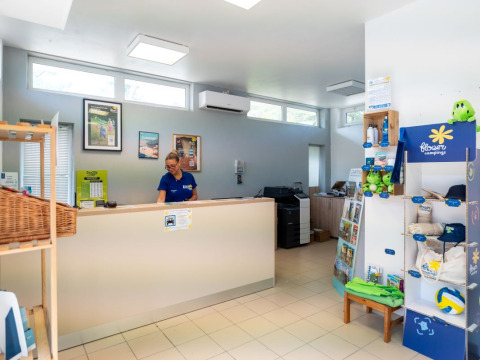 Receptie van Flower Camping Monplaisir, Nouvelle-Aquitaine, met medewerkster en campingartikelen.