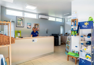 Recepción de Flower Camping Monplaisir con una empleada y estantería de artículos de campamento en venta.