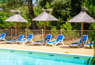 Buitenzwembad met blauwe ligzetels en rieten parasols bij Flower Camping Monplaisir, Nouvelle-Aquitaine, Frankrijk.