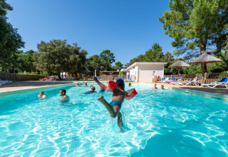 Børn leger i en udendørs swimmingpool på Flower Camping Monplaisir i Nouvelle-Aquitaine, Frankrig, omgivet af træer.