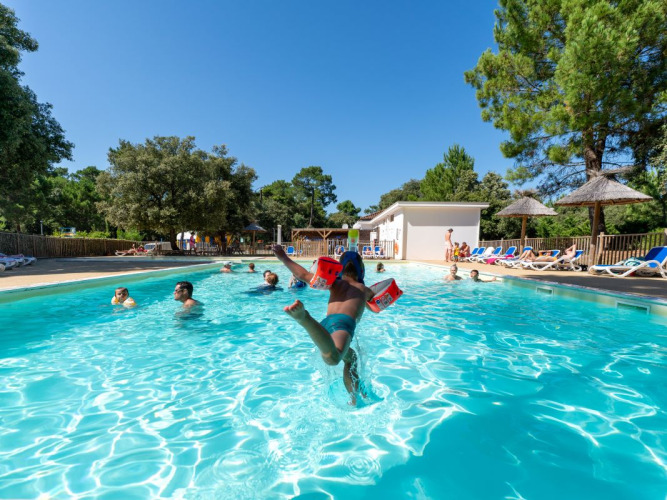 Niños jugando en la piscina al aire libre de Flower Camping Monplaisir en Nouvelle-Aquitaine, Francia, rodeados de árboles.