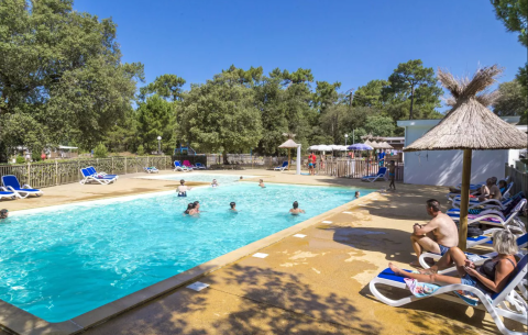 Udendørs swimmingpool med solbadende gæster og børn der leger, Flower Camping Monplaisir, Nouvelle-Aquitaine, Frankrig.