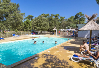 Buitenzwembad met zonnebaders en kinderen bij Flower Camping Monplaisir, Nouvelle-Aquitaine, Frankrijk.