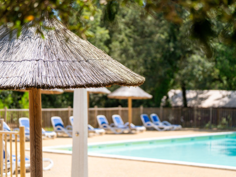 Swimmingpool med stråparasoller og blå liggestole i feriepark Flower Camping Monplaisir i Nouvelle-Aquitaine.