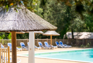 Piscina con sombrillas de paja y tumbonas azules en Flower Camping Monplaisir, Nouvelle-Aquitaine, Francia.