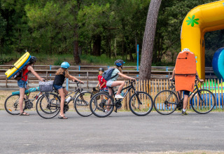 Familie mit Helmen und Schwimmbrettern auf Fahrrädern bei Flower Camping Monplaisir, Nouvelle-Aquitaine, Frankreich.