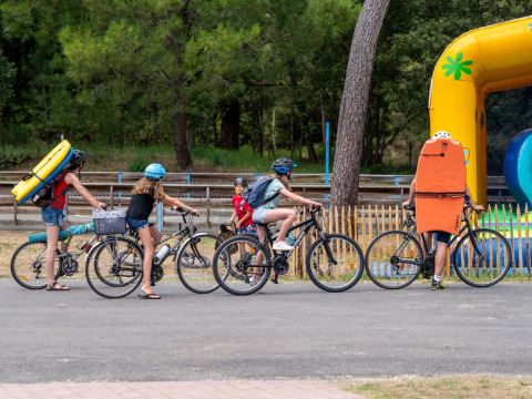 Familie på cykler med badeting på ryggen, klar til en dag i naturen ved Flower Camping Monplaisir, Frankrig.